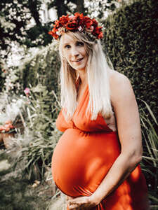 Schwangere Frau im roten Kleid mit Blumenkranz im Haar fotografiert im Garten